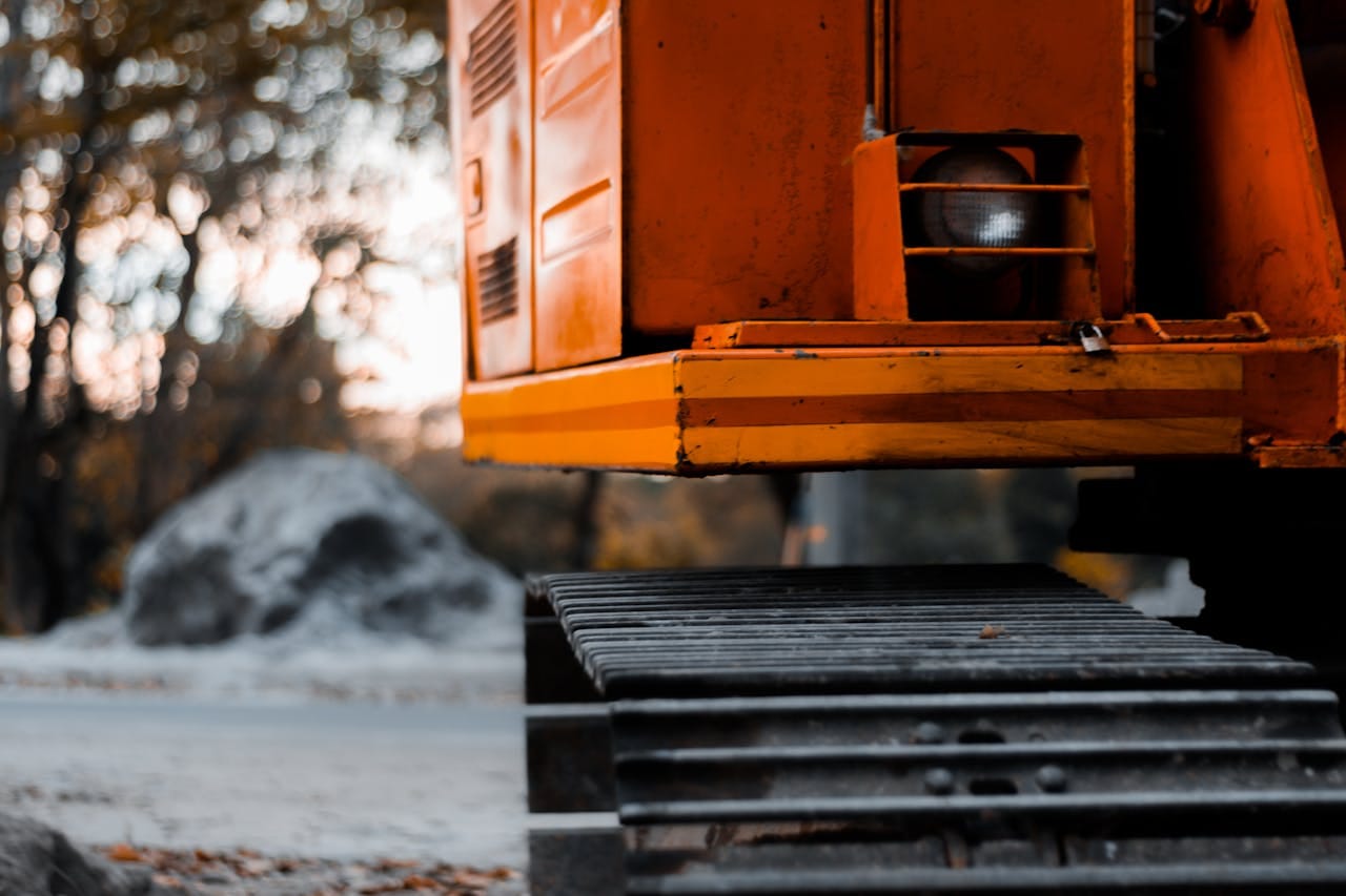 Close-up shot of an orange excavator with tracks in an outdoor setting during the day.